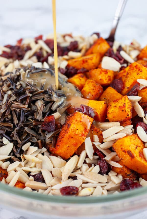 Maple mustard dressing poured onto harvest wild rice salad in glass bowl with spoon.