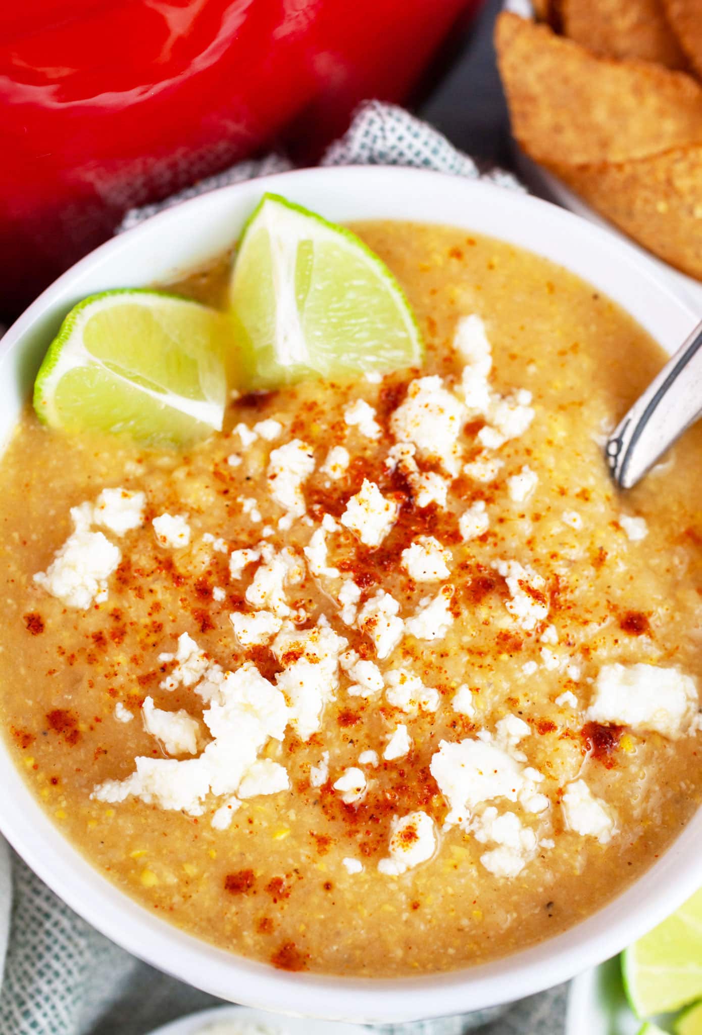 Southwest sweet corn cauliflower soup in white bowl with spoon garnished with queso fresco, chili powder, and lime wedges.