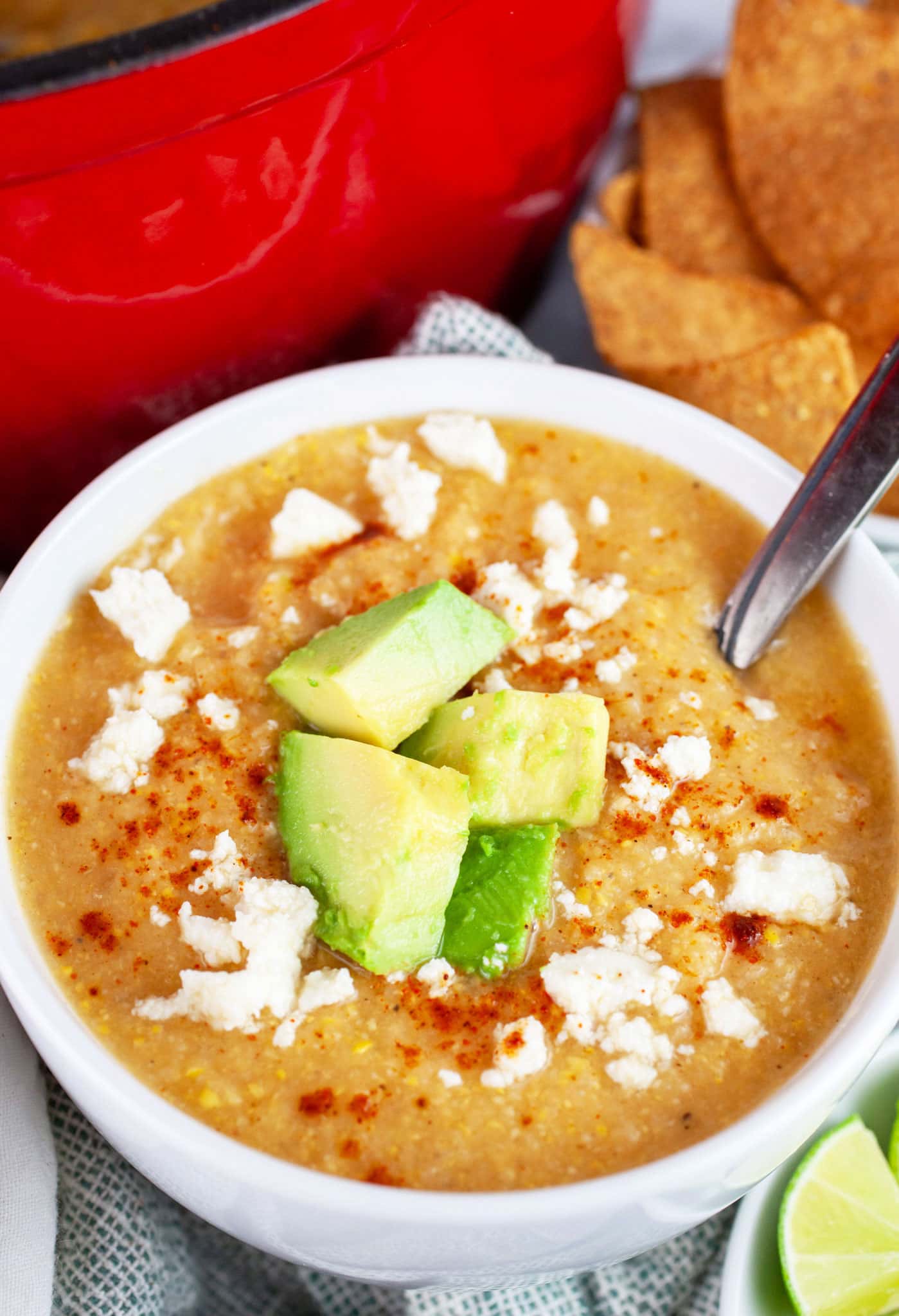 Southwest cauliflower corn soup garnished with diced avocadoes and queso fresco in white bowl with spoon.