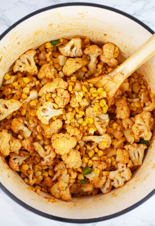 Sweet corn and cauliflower florets sauteed with spices in Dutch oven with wooden spoon.