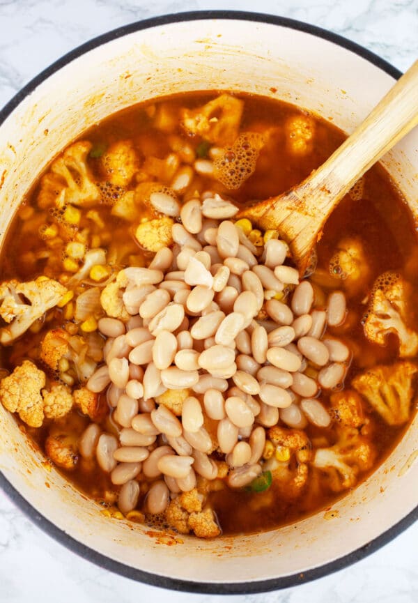 Cauliflower corn soup with cannellini beans in Dutch oven with wooden spoon.
