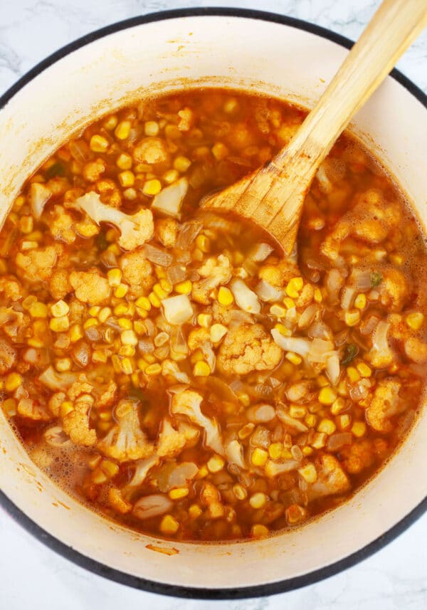 Uncooked corn cauliflower soup in Dutch oven with wooden spoon.