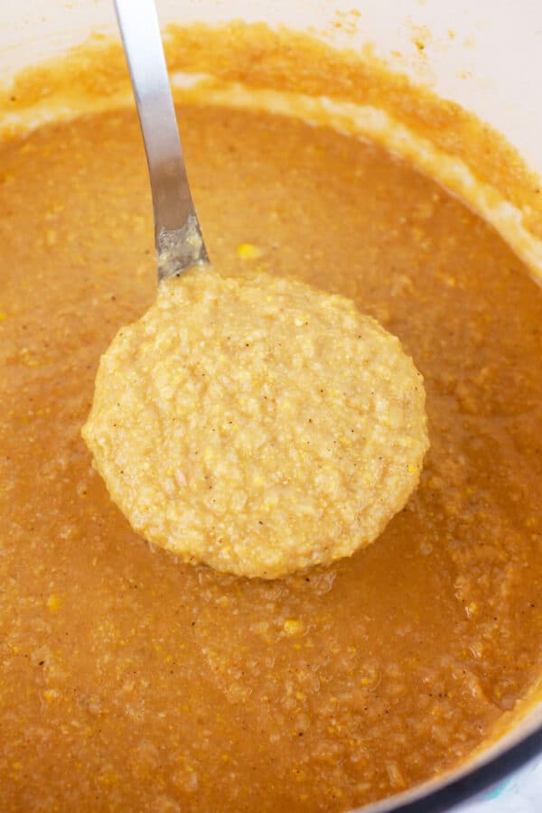 Scoop of cauliflower corn soup lifted from Dutch oven on metal ladle.
