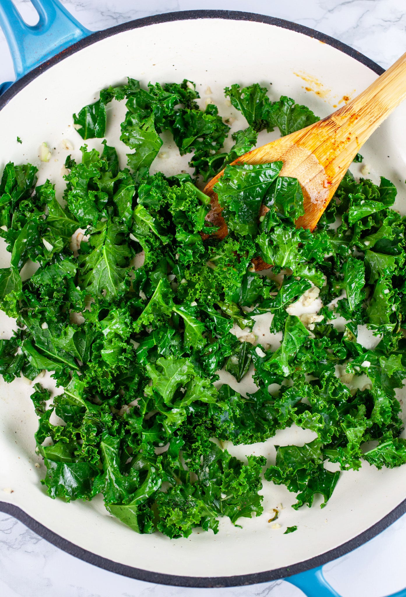 Sauteed kale in cast iron skillet with wooden spoon.