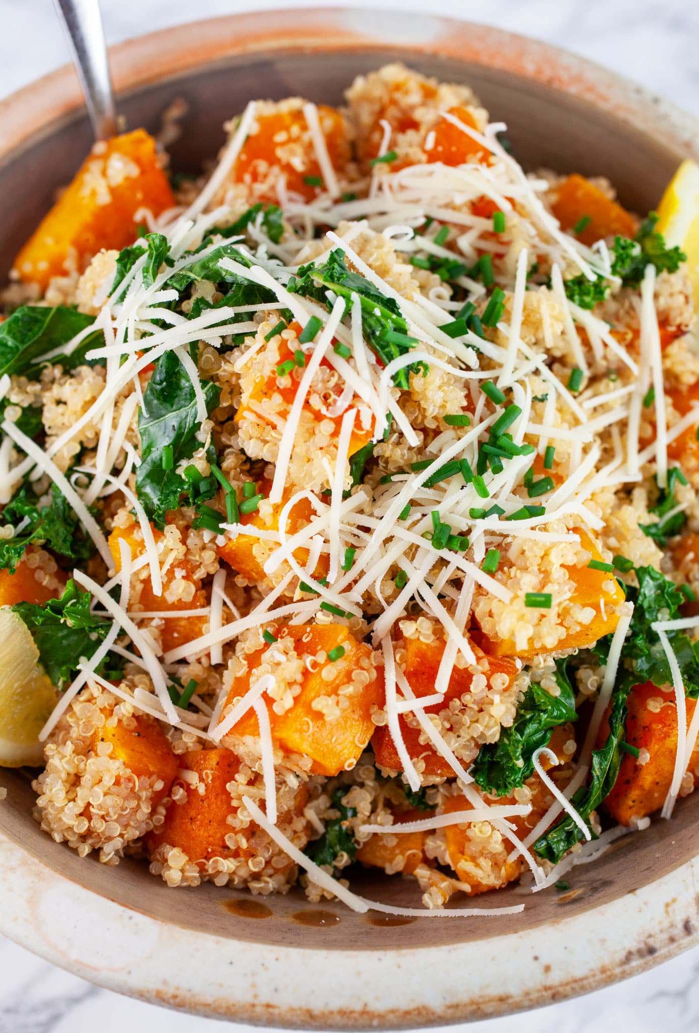 Butternut squash quinoa kale salad in ceramic bowl garnished with Parmesan cheese.