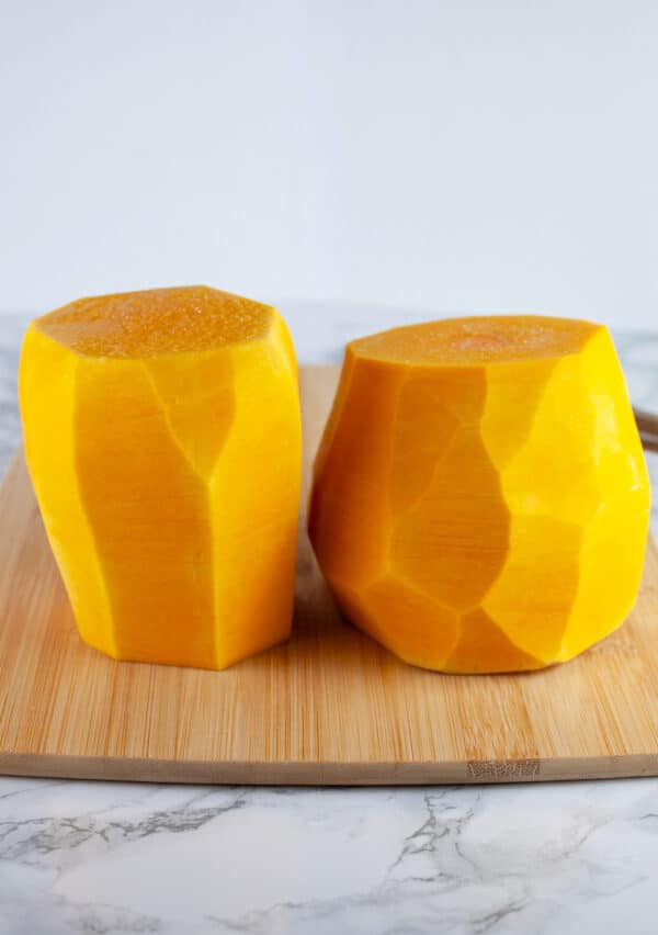 Butternut squash peeled and cut in half on wooden cutting board.