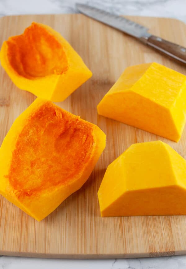 Butternut squash halves cut in half on wooden cutting board with knife.
