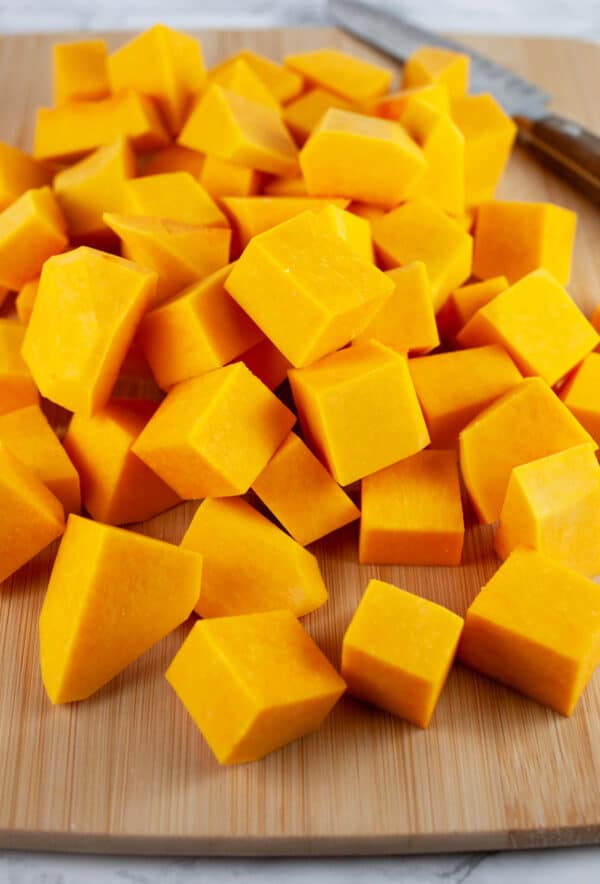 Butternut squash chunks on wooden cutting board with knife.