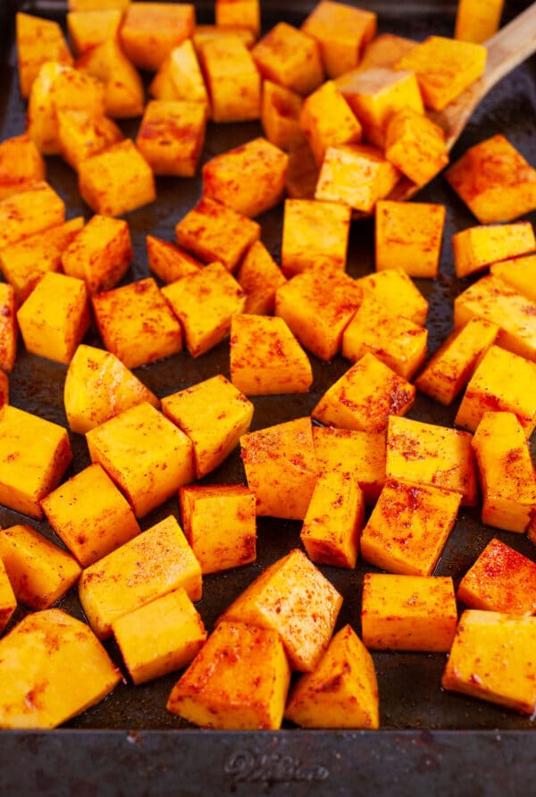 Uncooked, diced butternut squash tossed in olive oil and spices on baking sheet.