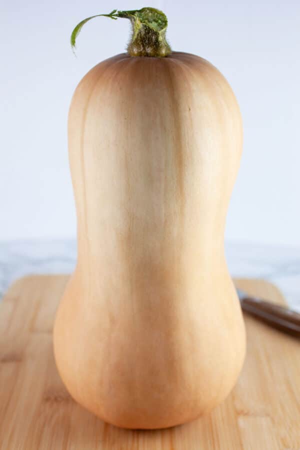 Whole butternut squash on wooden cutting board with knife.
