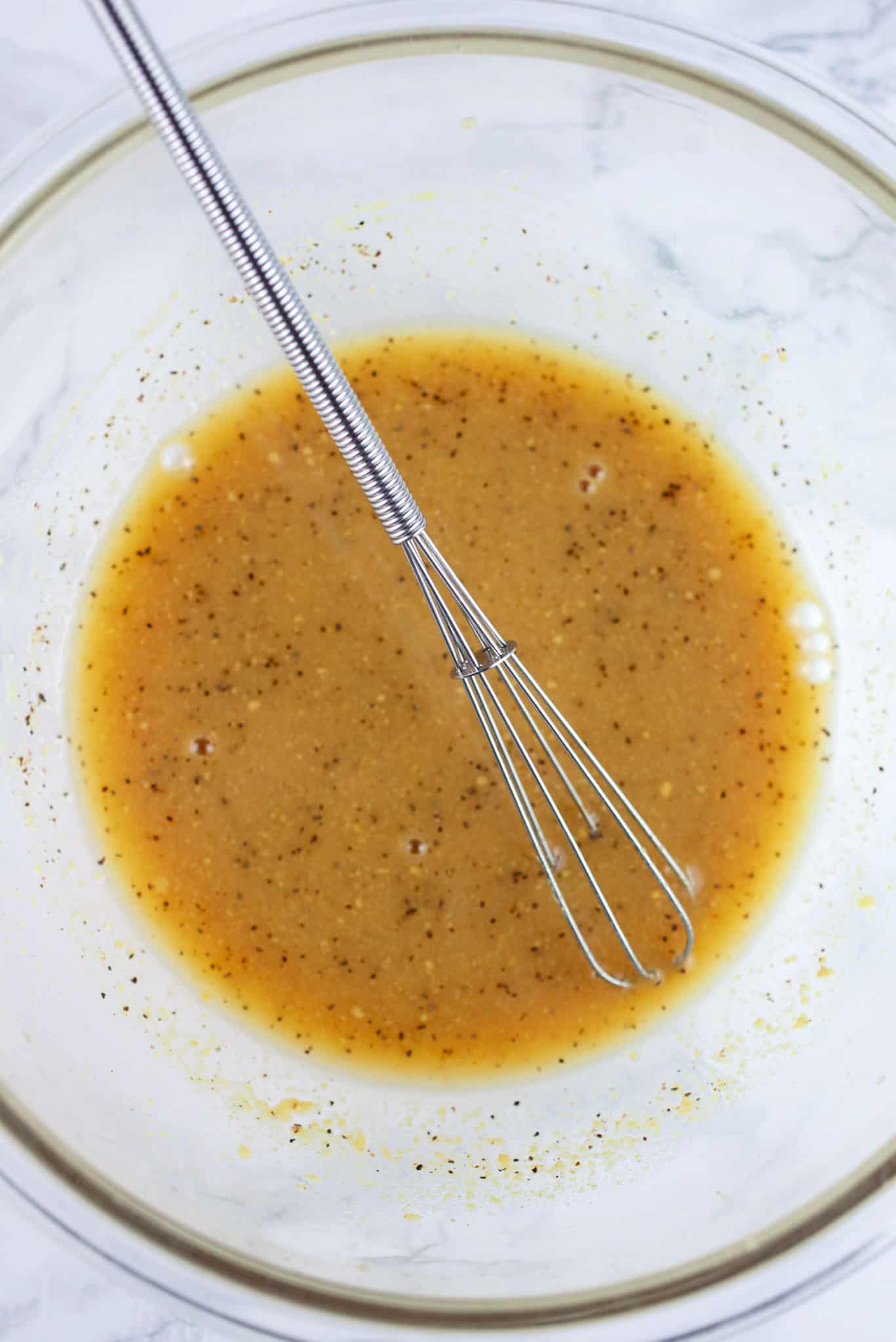 Maple mustard glaze in white bowl with small whisk.