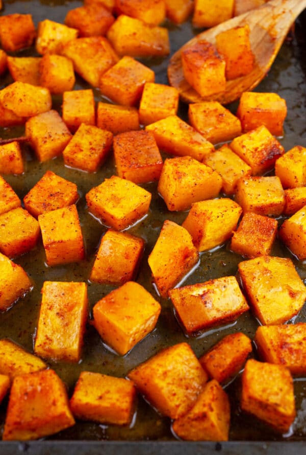 Roasted, diced butternut squash tossed in maple Dijon glaze on baking sheet.