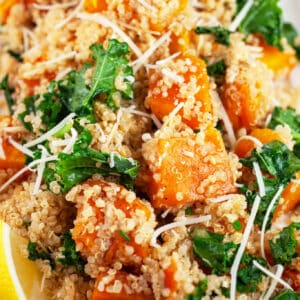 Butternut squash quinoa kale salad garnished with Parmesan cheese and lemon wedge.