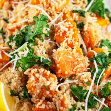 Butternut squash quinoa kale salad garnished with Parmesan cheese and lemon wedge.