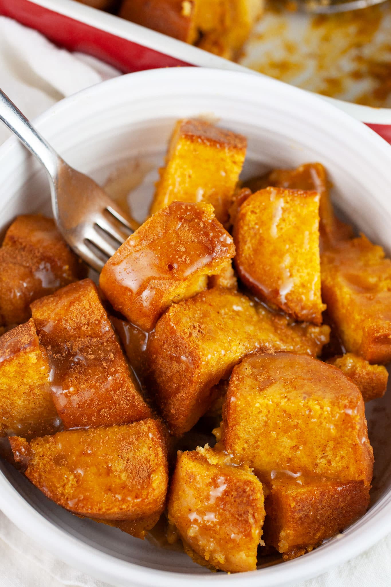 Pumpkin bread pudding with caramel sauce in white bowl with spoon.