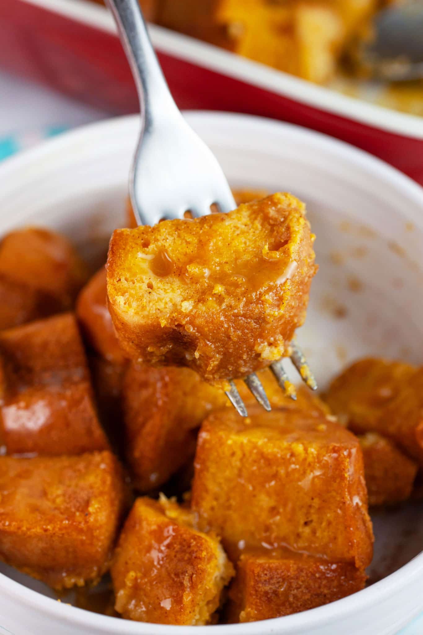 Pumpkin bread pudding lifted with fork from white bowl.