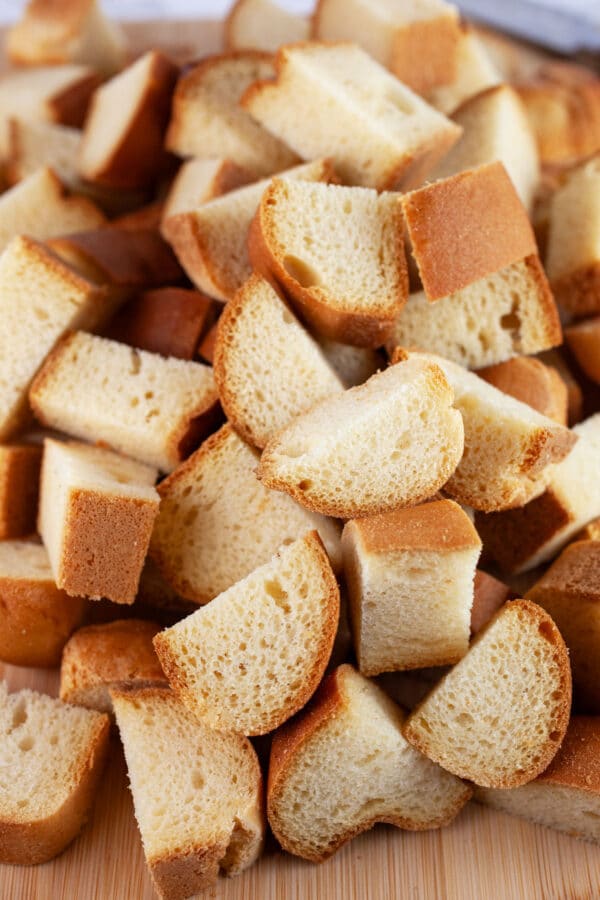 Brioche bread cubes on wooden cutting board with knife.