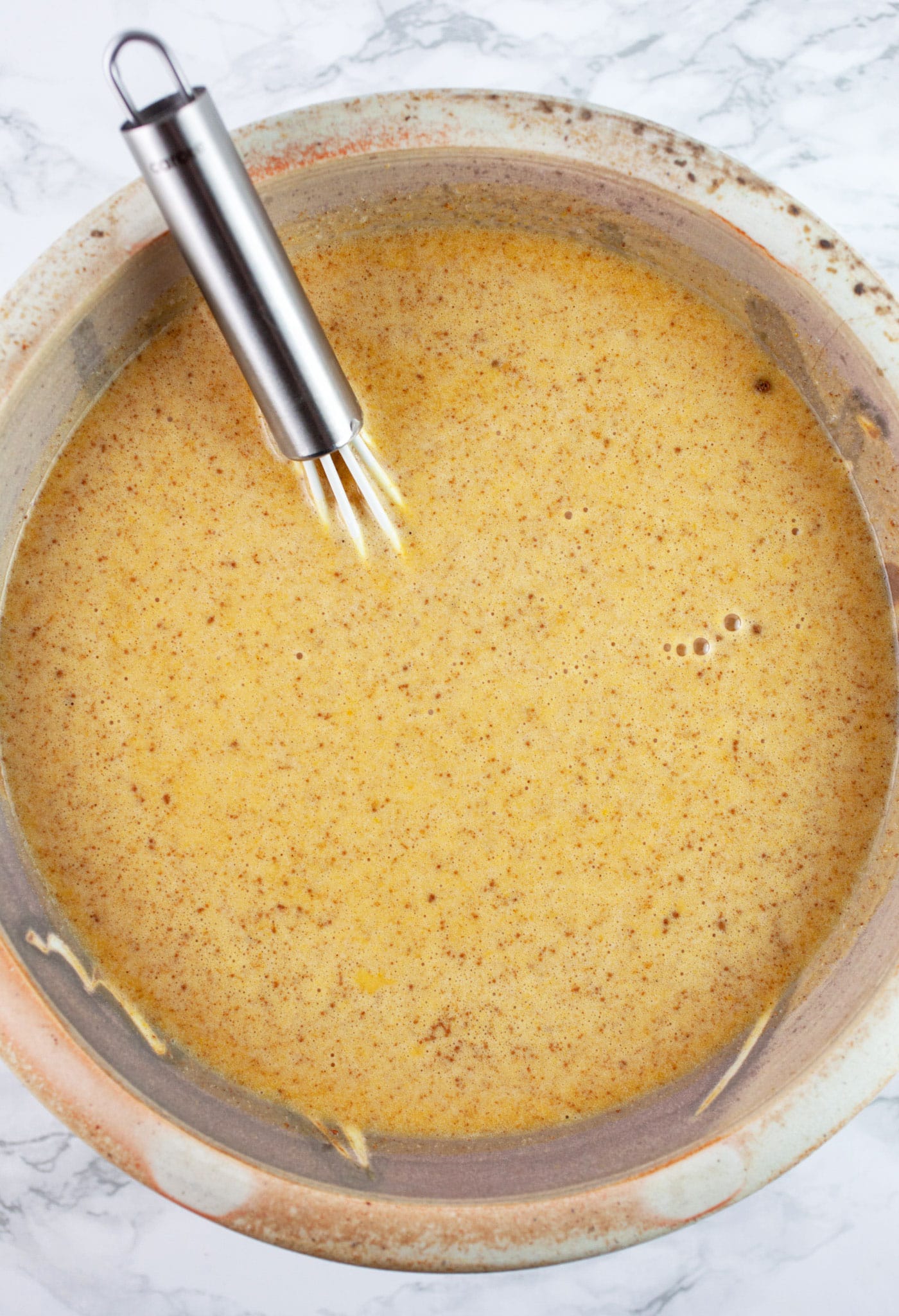 Pumpkin custard in ceramic bowl with whisk.