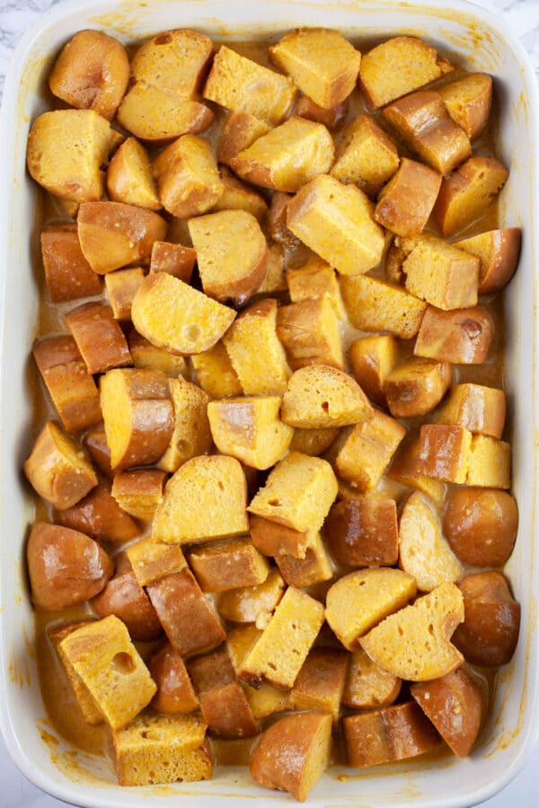 Uncooked bread cubes soaking in pumpkin custard in ceramic baking dish.