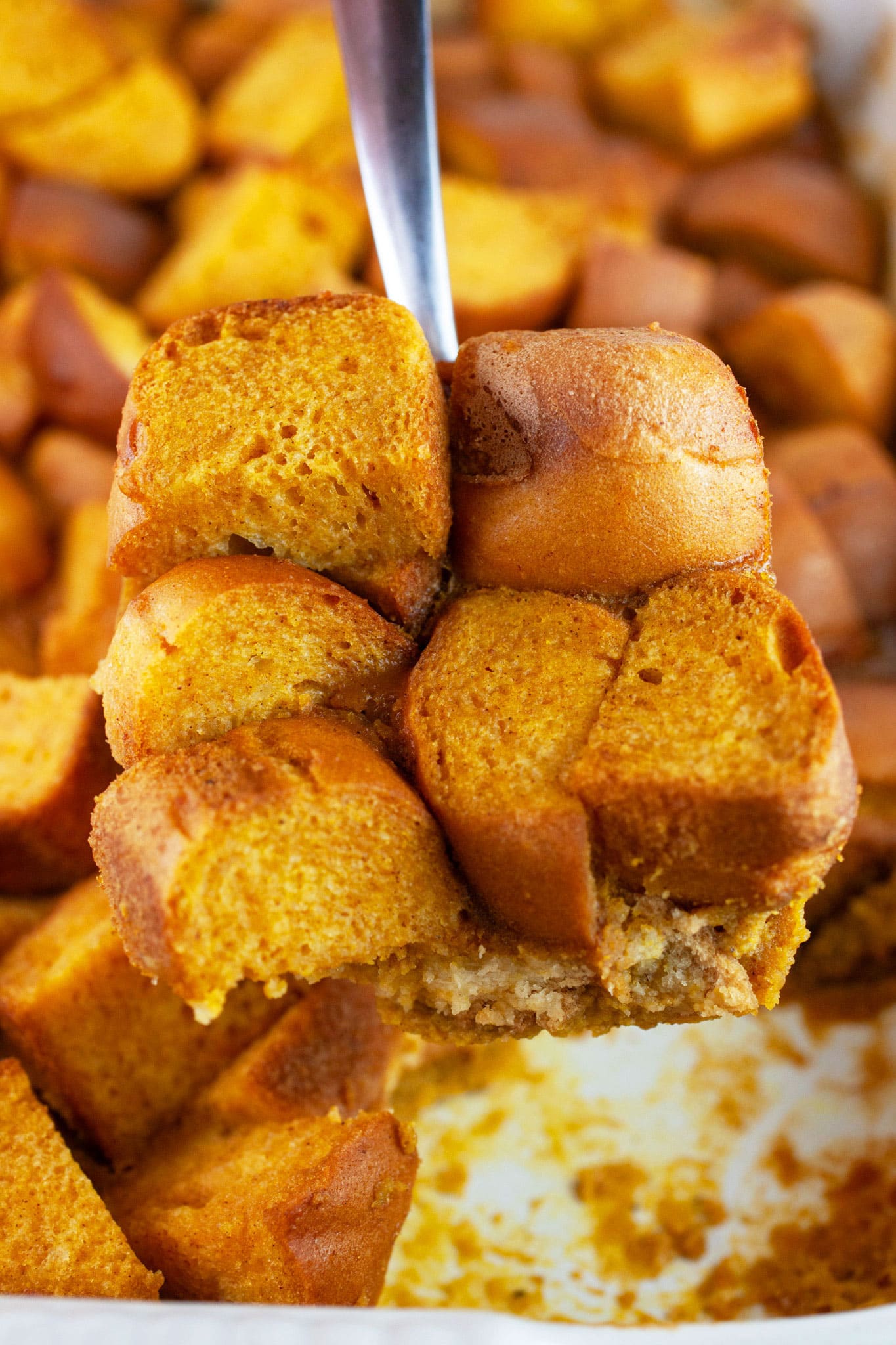 Slice of pumpkin bread pudding lifted from baking dish on metal spoon.