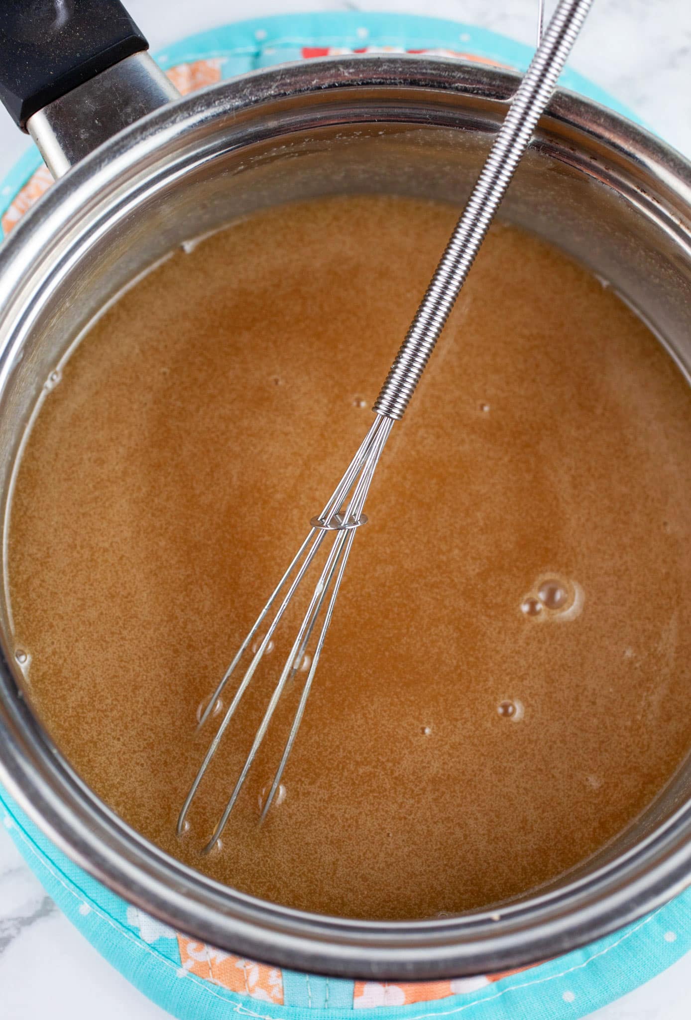 Caramel sauce in sauce pan with small whisk.
