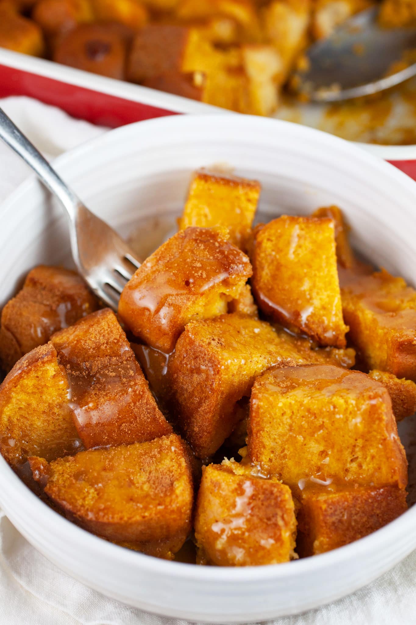 Pumpkin bread pudding with caramel sauce in white bowl with fork.