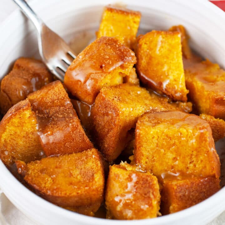 Pumpkin bread pudding with caramel sauce in white bowl with fork.