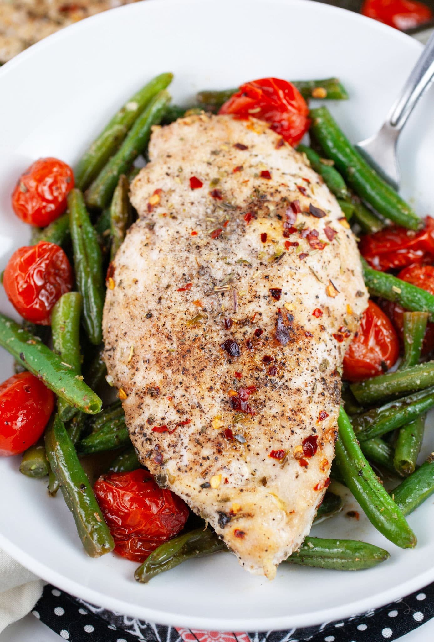Roasted Italian chicken with green beans and tomatoes in white bowl with fork.