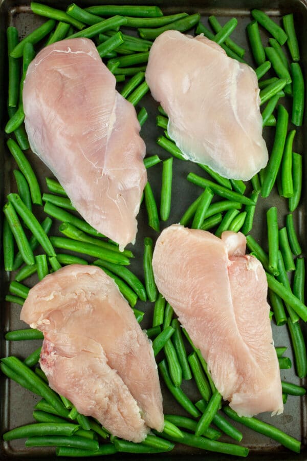Raw chicken breasts and green beans on baking sheet.
