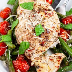 Sheet pan Italian chicken breast with green beans and tomatoes garnished with Parmesan cheese and fresh basil.