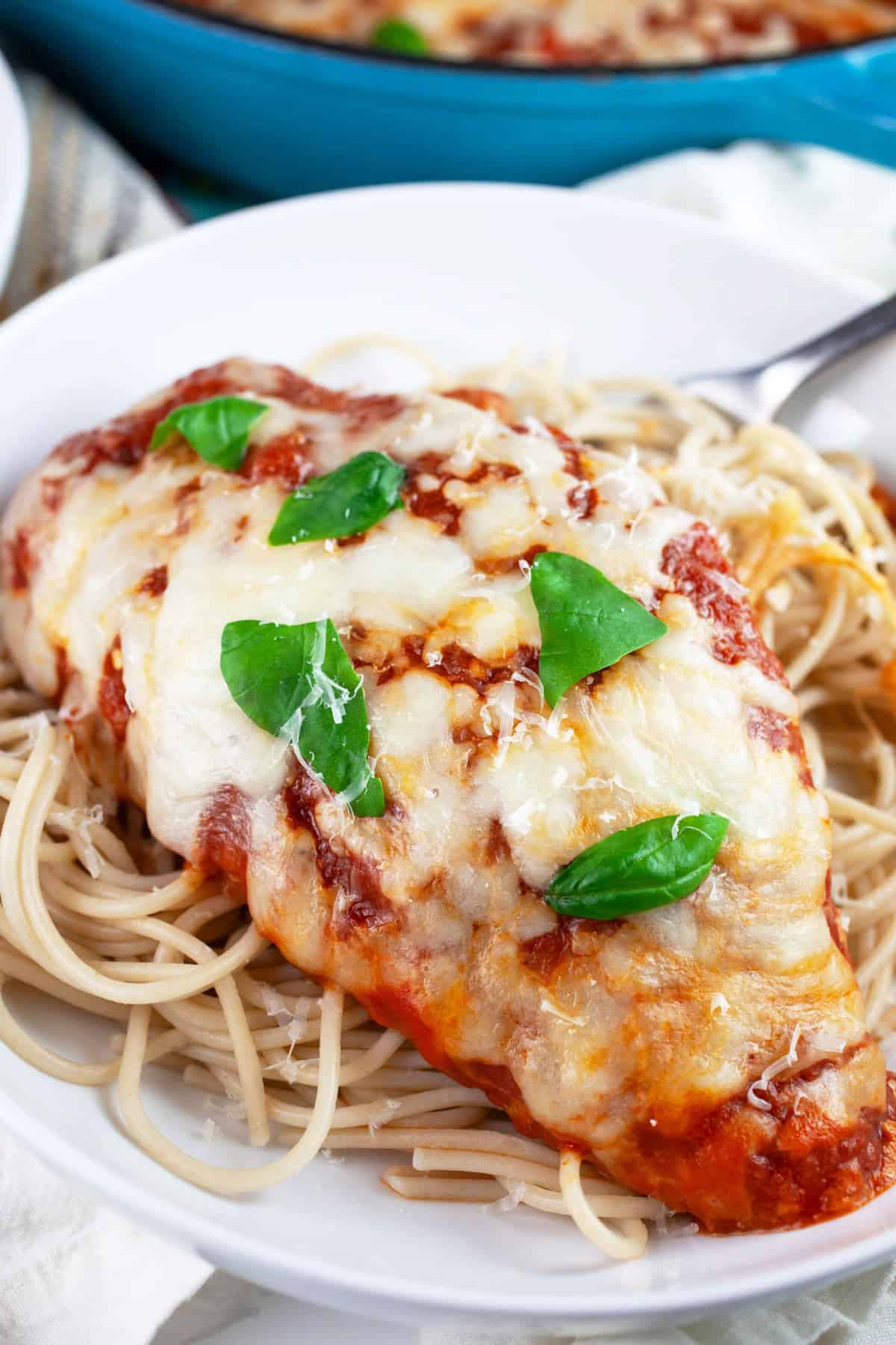 Gluten free chicken Parmesan in white bowl with spaghetti noodles and garnished with fresh basil.