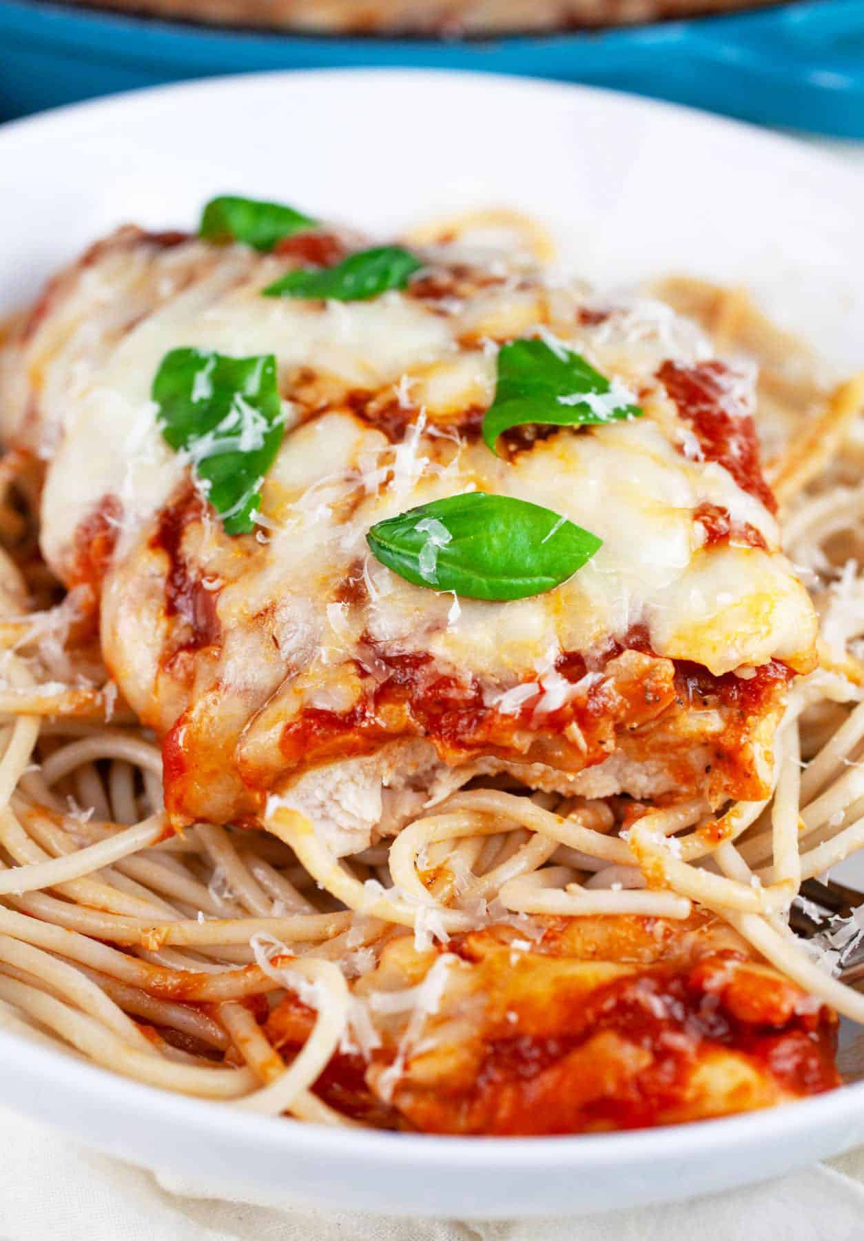 Gluten free chicken Parmesan with spaghetti noodles garnished with fresh basil in white bowl.