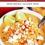 Sweet corn cauliflower soup garnished with queso fresco and lime wedges in white bowl with spoon.