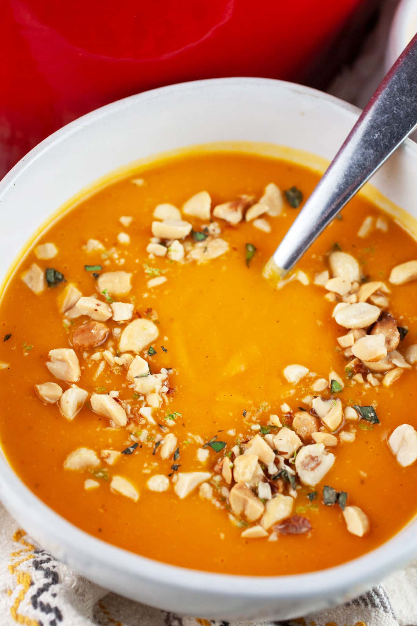 Thai butternut squash soup with peanut topping in white bowl with spoon.