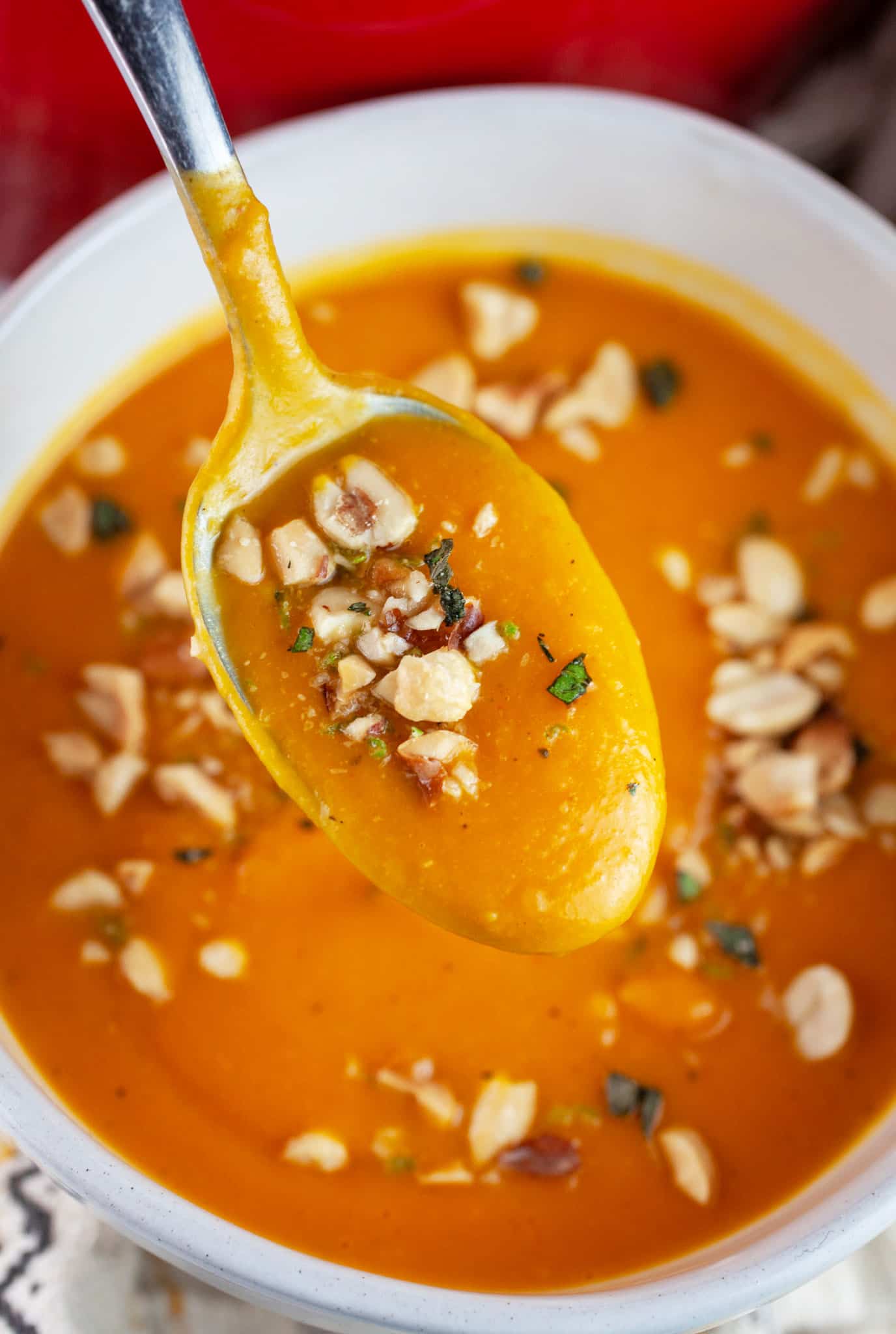 Spoonful of curried butternut squash soup garnished with peanuts lifted from white bowl.