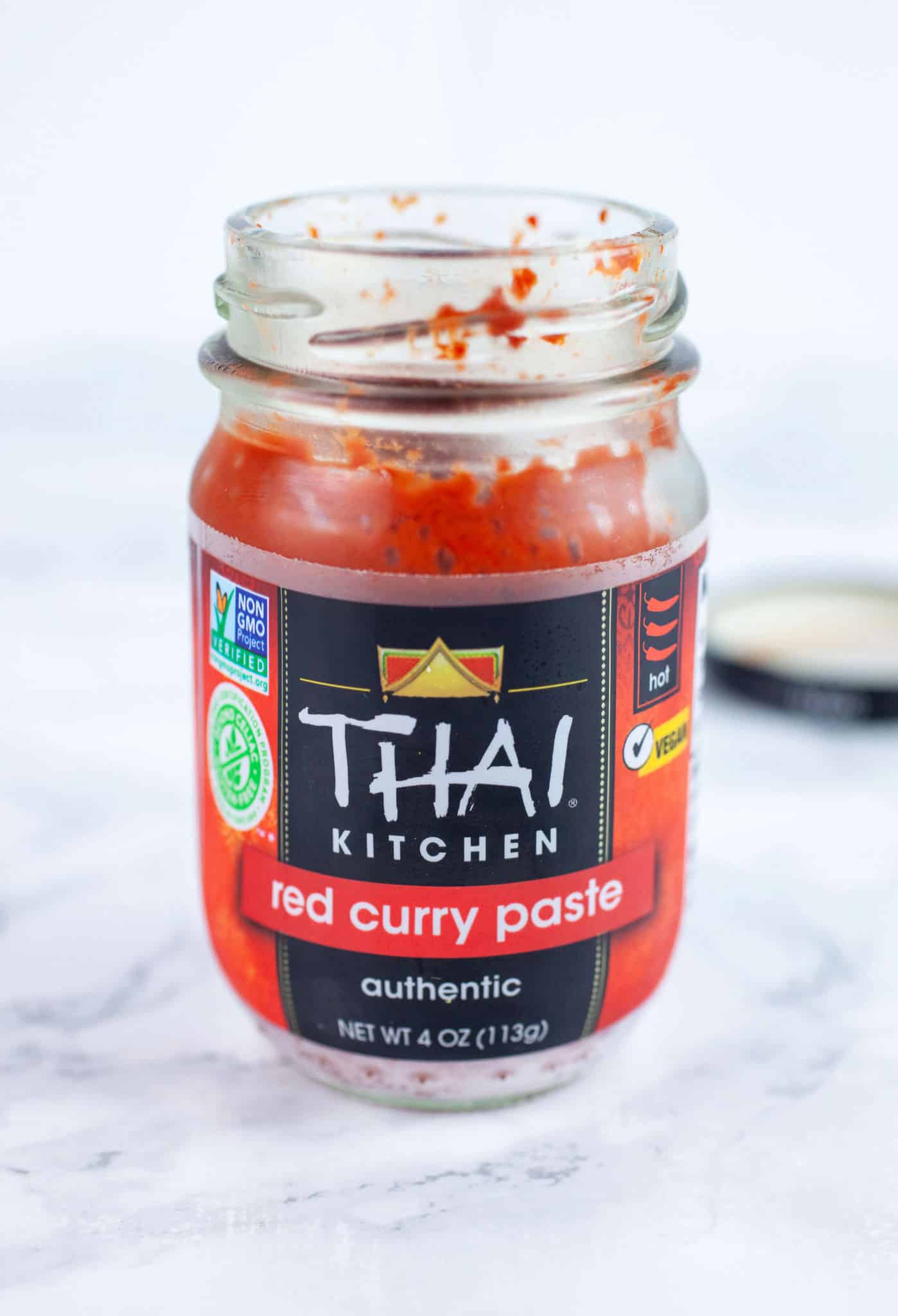 Opened jar of Thai red curry paste on white surface.