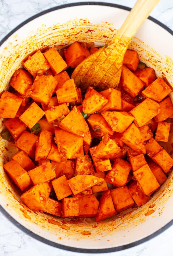 Diced butternut squash sauteed with red chili paste in Dutch oven with wooden spoon.