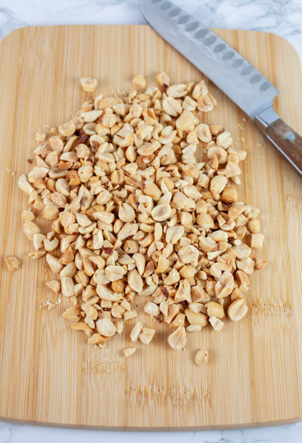 Chopped dry roasted peanuts on wooden cutting board with knife.