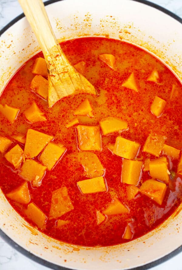 Uncooked butternut squash soup in Dutch oven with wooden spoon.