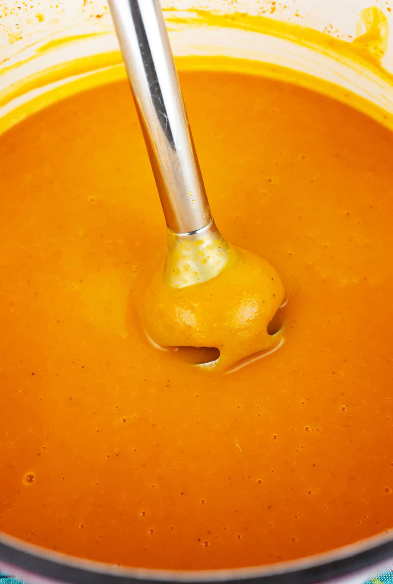 Immersion blender with pureed curried butternut squash soup in Dutch oven.