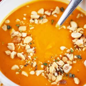 Curried butternut squash soup with peanut topping in white bowl with spoon.