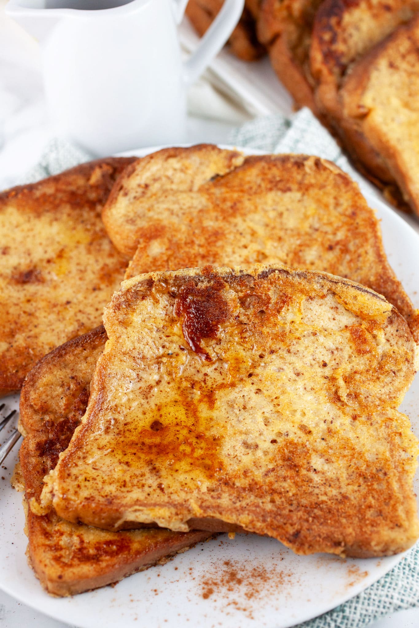 Eggnog French toast on white plate next to dish of maple syrup.