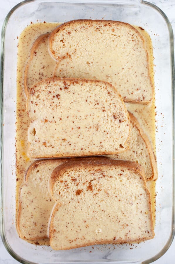 Sliced bread and custard in glass cake pan.