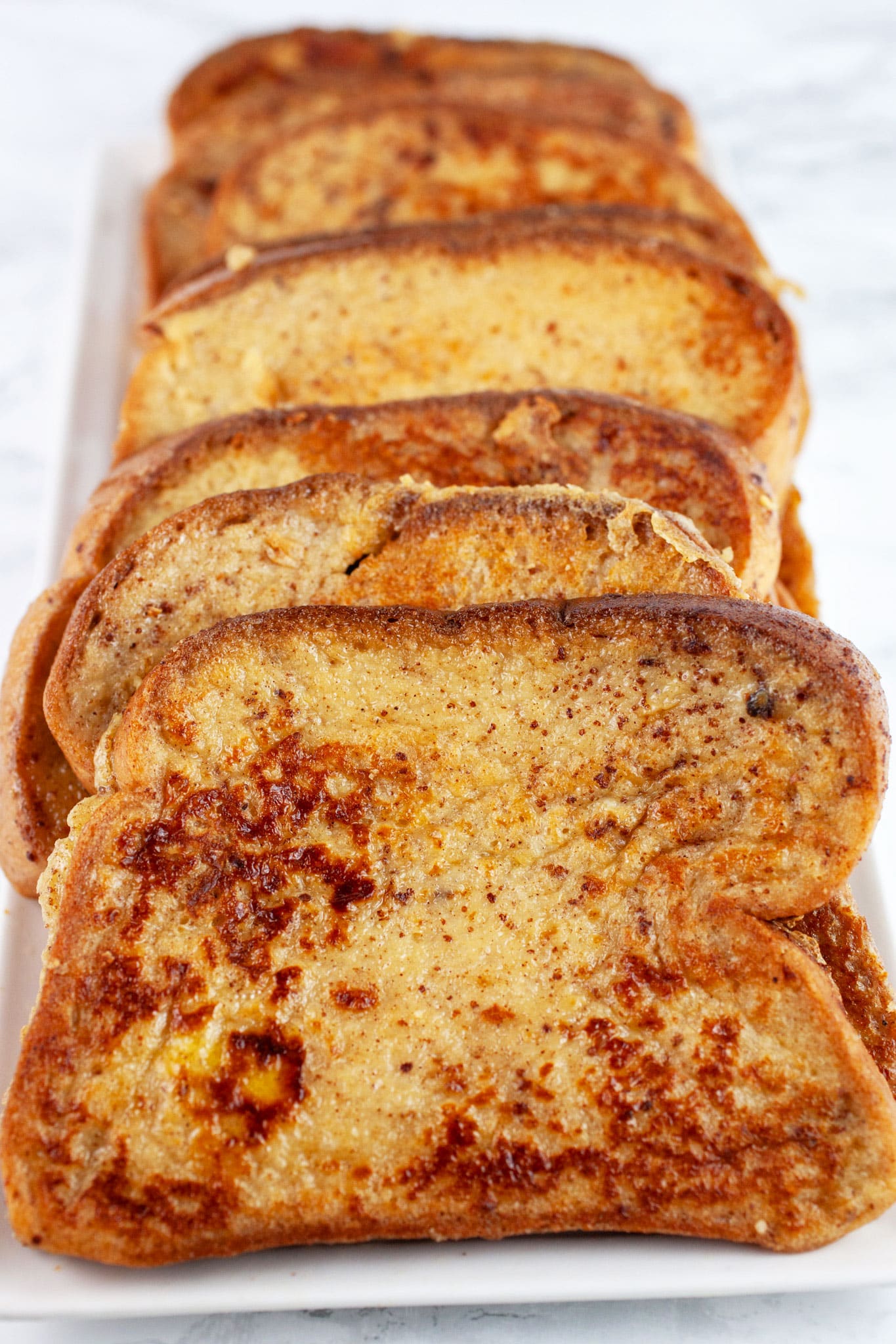 Eggnog French toast lined up on white platter.