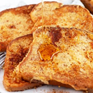 Maple syrup poured onto eggnog French toast on white plate with fork.