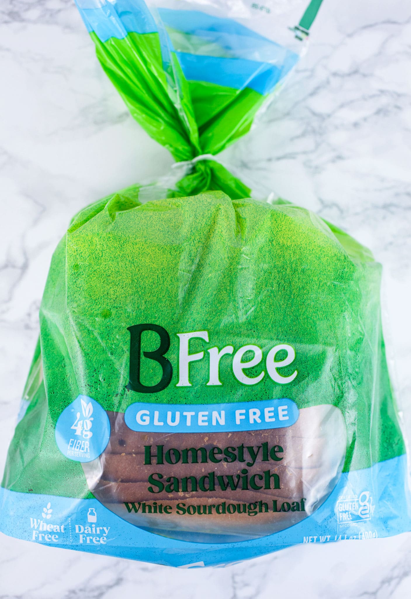 Unopened package of sliced gluten free sourdough bread on white surface.