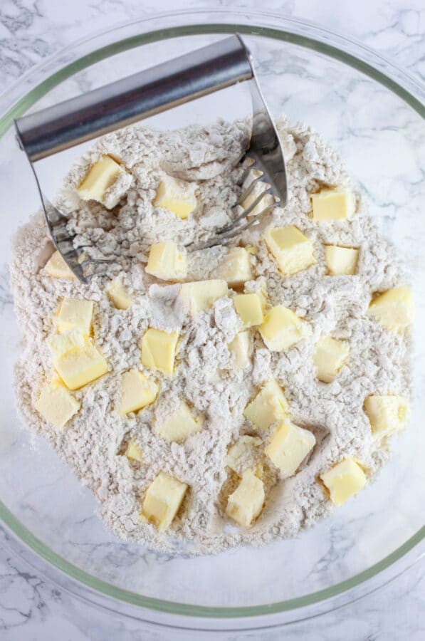 Gluten free flour blend and chunks of cold butter in large glass bowl with pastry cutter.