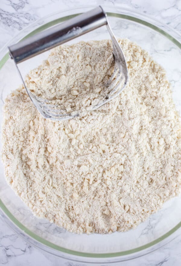 Gluten free flour and butter combined in large glass bowl with pastry cutter.