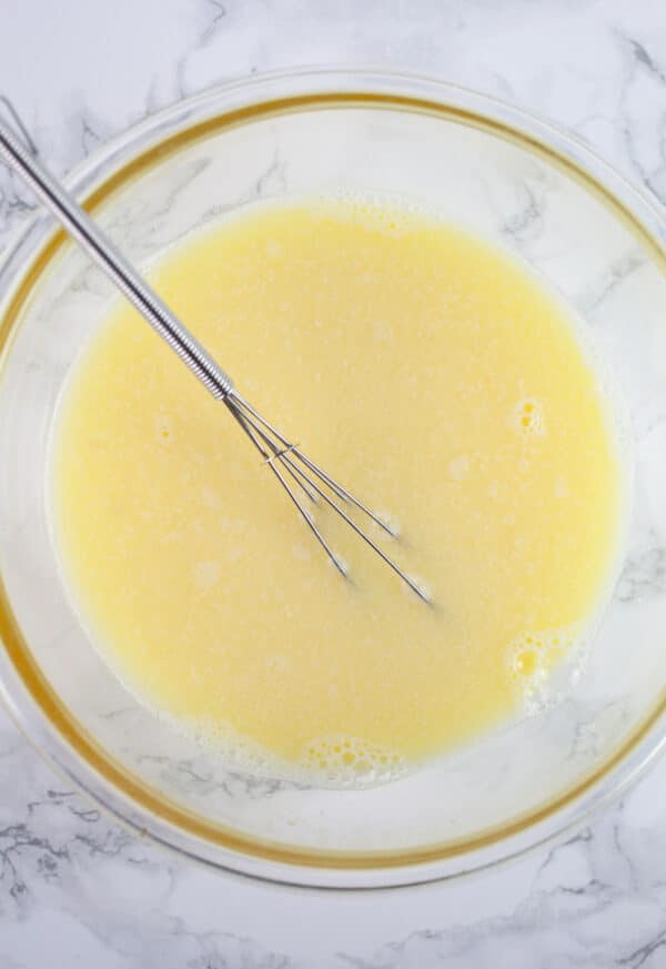 Egg and water combined in glass bowl with small whisk.