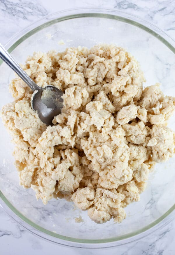 Pie dough combined in large glass bowl with spoon.